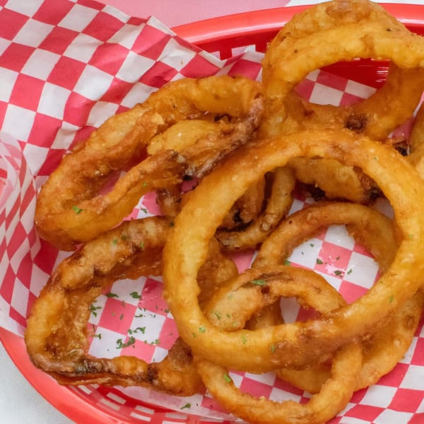 Golden-brown onion rings with parsley flakes in a red basket with red and white checkered paper.