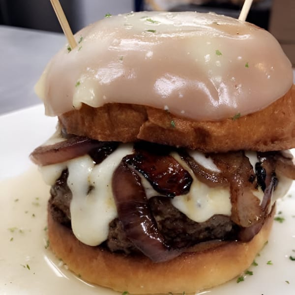 Rock Burger's burger with melted cheese, caramelized onions, and a glazed bun, served on a white plate.