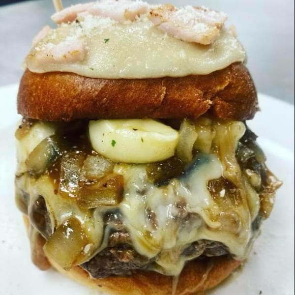 Close-up of a Rock Burger with melted cheese, caramelized onions, and garlic cloves.