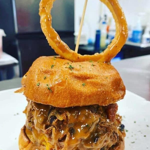 A Rock Burger with pulled pork, melted cheese, and a large onion ring on top.