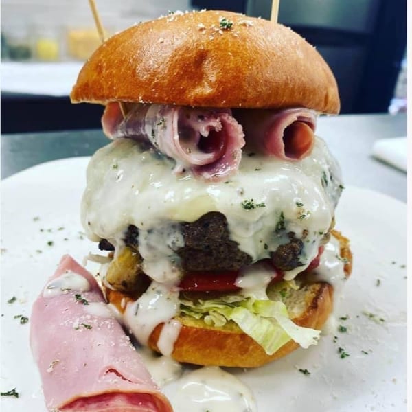 A Rock Burger with melted white cheese, ham, lettuce, and tomato on a bun.