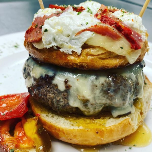 A Rock Burger with melted cheese, bacon, and a creamy white topping, served with roasted peppers.