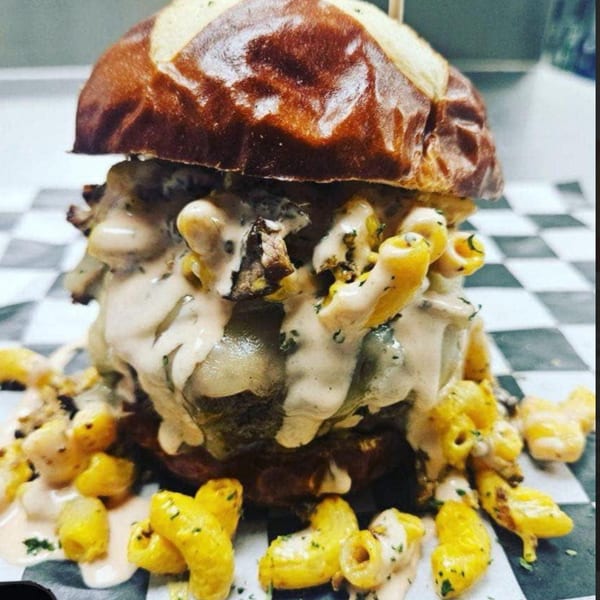 A Rock Burger with a pretzel bun, overflowing with mac and cheese and creamy sauce.