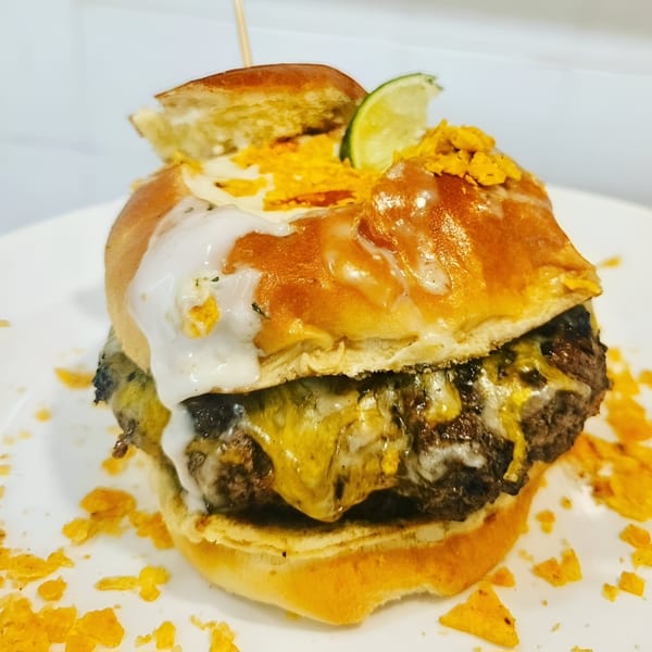 Rock Burger's cheesy burger with white sauce, crushed chips, and a lime wedge on a white plate.