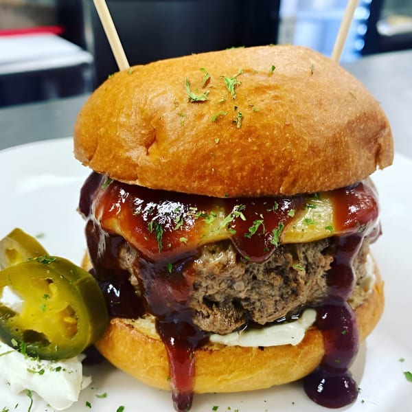 Rock Burger's juicy burger with melted cheese, BBQ sauce, and jalapeños on a toasted bun.