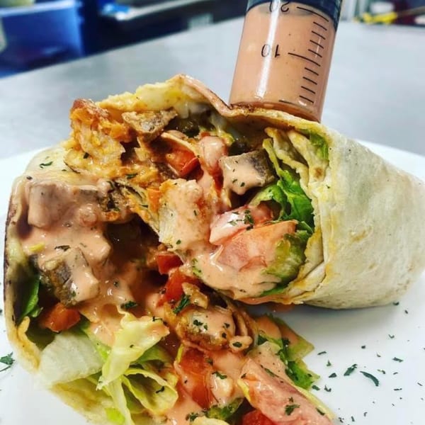 Rock Burger's chicken wrap, filled with lettuce, tomatoes, and sauce, with a sauce syringe.