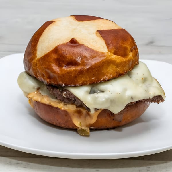 Rock Burger's cheeseburger with melted cheese and sauce on a pretzel bun, served on a white plate.