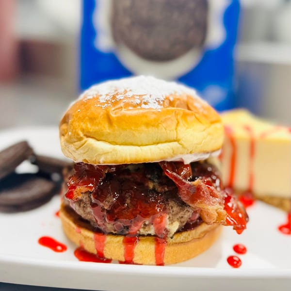 Rock Burger's sweet burger with powdered sugar, bacon, and red sauce, next to cheesecake and cookies.