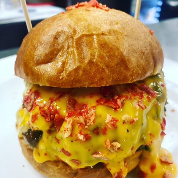 Rock Burger's cheesy burger with melted yellow cheese and red crispy toppings on a white plate.