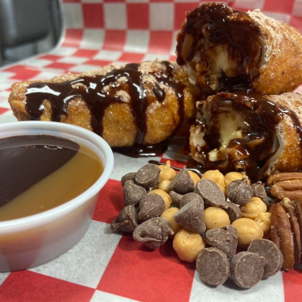 Fried dessert rolls drizzled with chocolate sauce, served with a dipping cup, chocolate chips, and pecans.