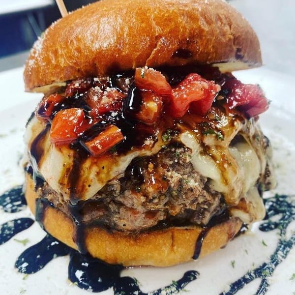A Rock Burger with melted cheese, diced tomatoes, and a dark balsamic glaze on a white plate.