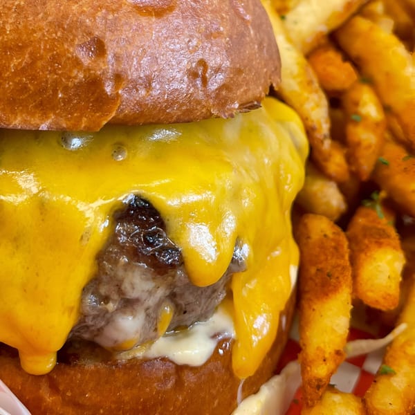 Close-up of a Rock Burger cheeseburger with melted cheese and a side of seasoned fries.