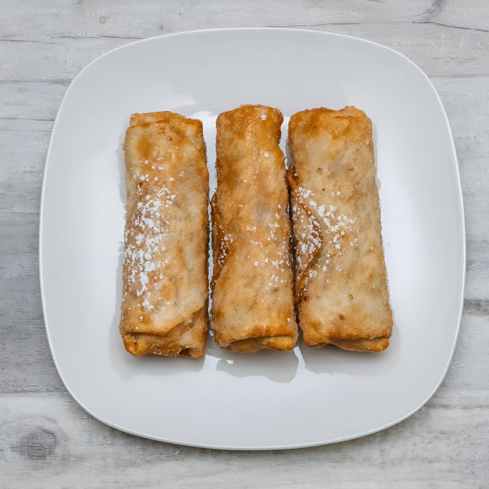 Three golden-brown fried spring rolls, lightly dusted with powdered sugar, on a white rectangular plate.
